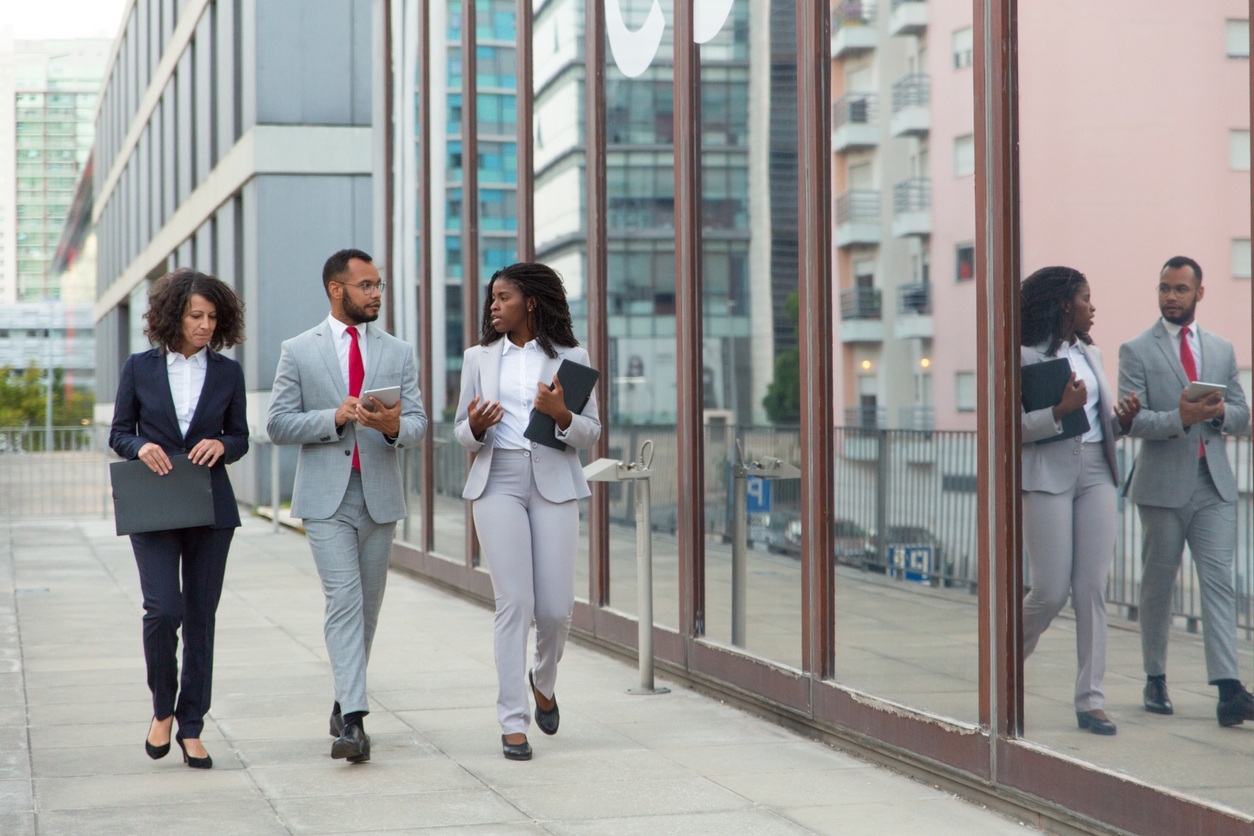 Three business colleagues discussing project on their way to office. Business man and woman walking outside in city. Corporate discussion concept