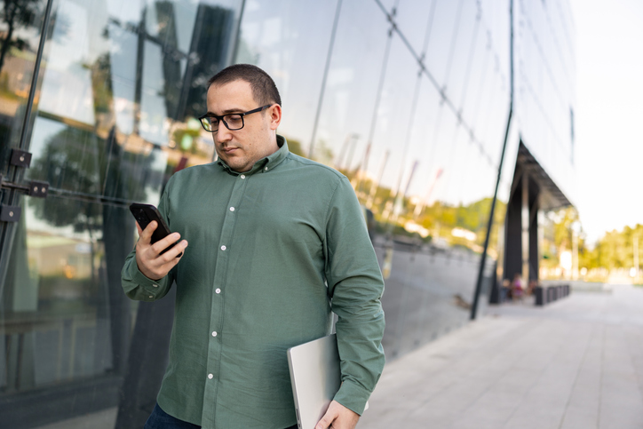 Man checking messages on smartphone outside a modern office building