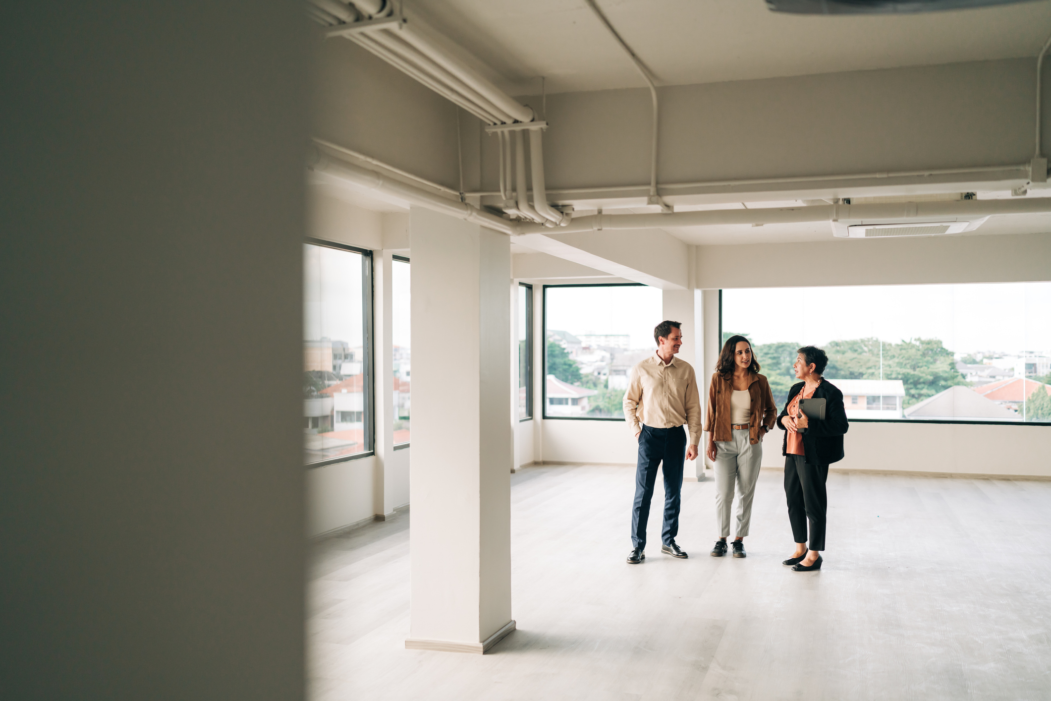 Experienced Asian real estate agent presenting empty apartment to multicultural couple